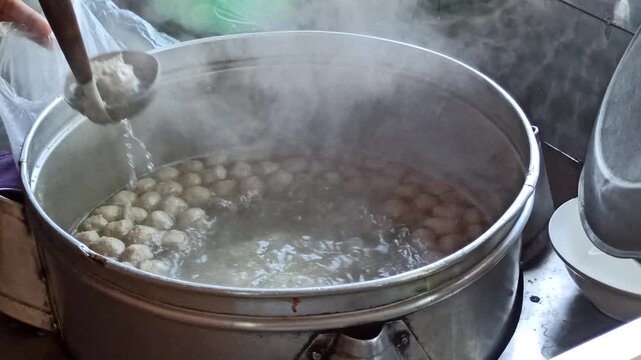 Large cooking pot filled with steaming meatball soup and assorted meatballs, showcasing authentic Indonesian culinary tradition.