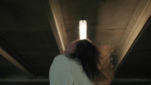 A stylish young woman dances with passion and energy in a dimly lit underground car park.