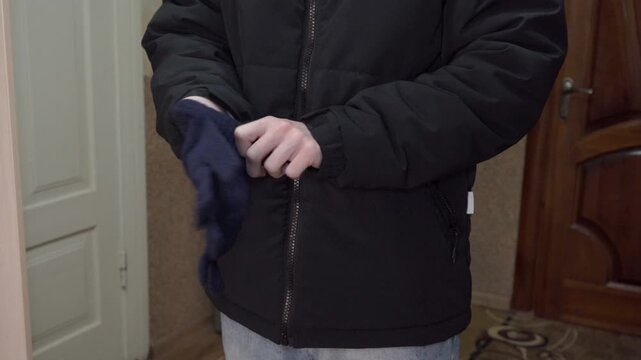 Man putting on blue winter knit gloves indoors , Man in black down jacket preparing for cold weather by putting on gloves.