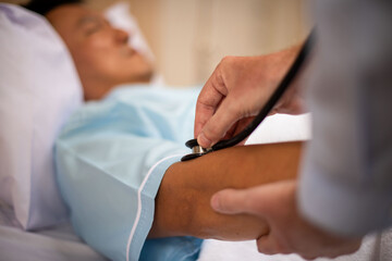 Doctor using a stethoscope on a patient's arm in a hospital bed.