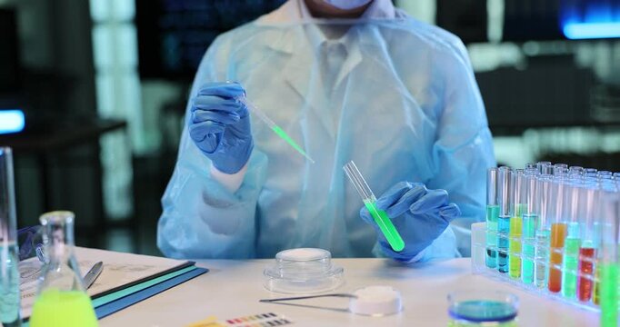 Researcher carefully pours bright green liquid onto microscope slide using pipette. Diligent laboratory specialist prepares sample for analysis