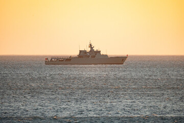 Obraz premium Military vessel sailing on calm water during sunset near the coast