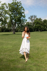 Obraz premium Girl in white dress holds strawberry and wants to eat it. Fragile Asian woman on picnic in park at dawn, summer vacation and outdoor recreation