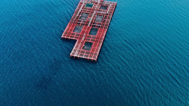 Red grid fish farm structure on open Black Sea water, Bulgaria. Aerial view of rectangular orange lattice aquaculture cage centered on deep blue sea, no land visible.