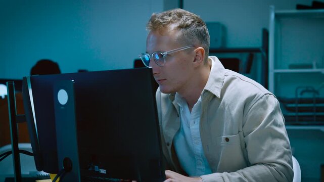 Young male IT specialist putting on glasses while working on computer software development data analysis and programming code in modern office room