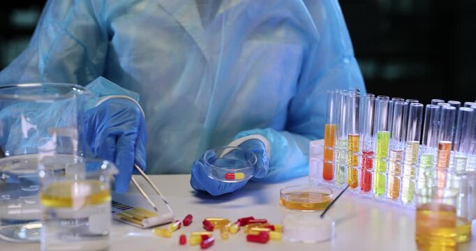 Lab technician transfers drug tablets onto Petri dish using laboratory tweezers. Laboratory assistant prepares samples for further scientific analysis