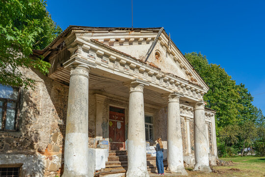 Female tourist exploring ruined 19th-century Zavishey estate outbuilding with columns in Kukhtichi, Belarus