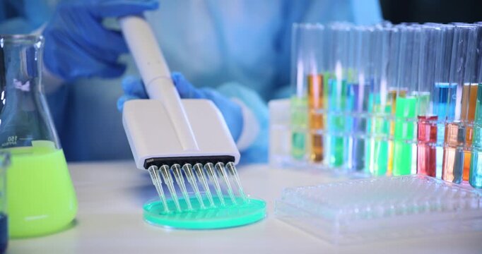 Laboratory specialist fills test tubes with vivid experimental liquid using professional automatic dispenser. Chemist uses lab multichannel pipette