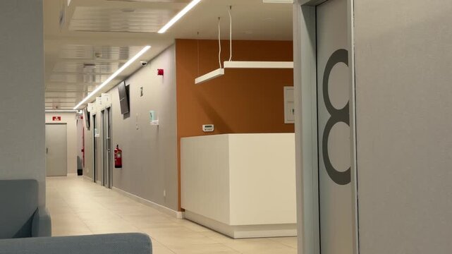 Madrid, Spain, June 9-2026: Interior view of a modern hospital corridor with reception desk, numbered consultation rooms, clean architectural design, and linear ceiling lighting. Healthcare facility e