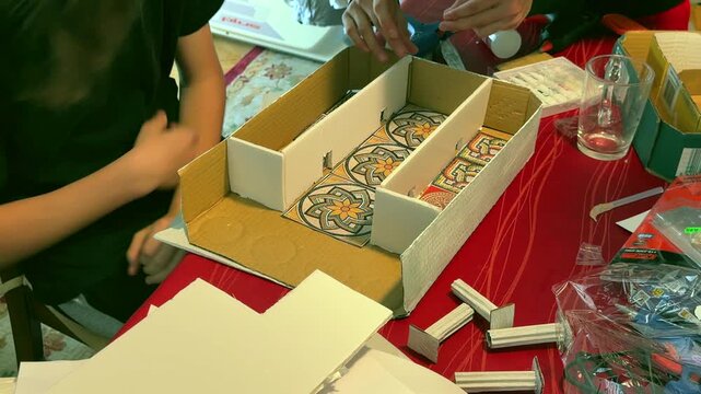 Madrid, Spain, June 9-2026: Close-up of students assembling a Roman house model from cardboard and printed decorative elements during a school history project. Hands working on an educational craft ac