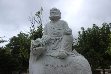 Obraz premium Large white marble statue of seated monk riding mythical animal in temple garden.