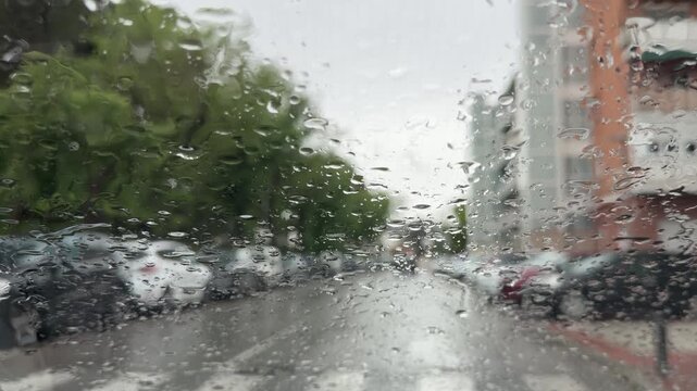 Madrid, Spain, June 9-2026: Close-up view through a rain-covered windshield with water droplets in focus and an urban street blurred in the background. Atmospheric rainy weather scene in a city enviro