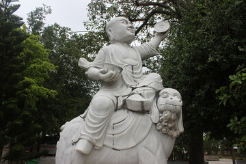Obraz premium Marble statue of monk riding mythical beast in sunny tropical garden of temple site.