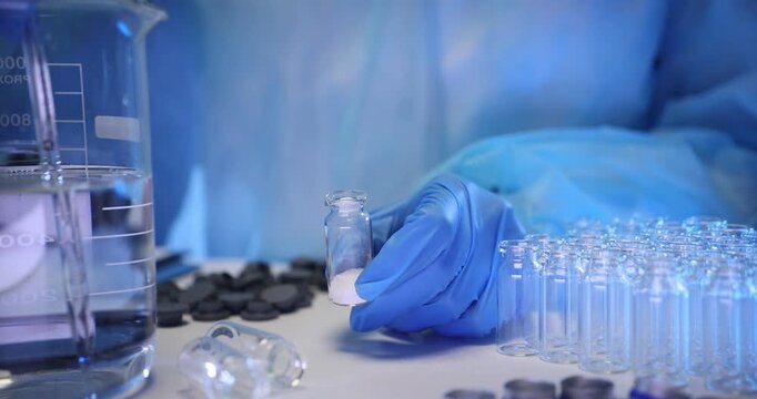 Scientific worker pours transparent substance into small glass bottle with poder drug using pipette. Lab technician conducts scientific analysis