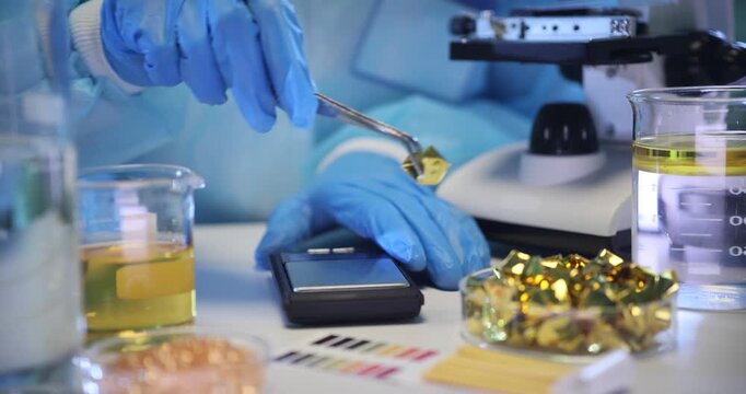 Researcher places pieces of shiny gold onto laboratory scales. Lab worker determines exact weight of golden fragments in scientific laboratory