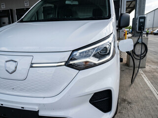 Fototapeta premium Front Detail of White Electric Van Charging at Outdoor Station in Industrial Setting