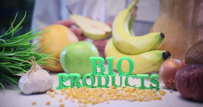 Bio Products text against fresh fruits and vegetables on doctor desk. Woman medic holds pear half as recommends healthy nutrition in hospital