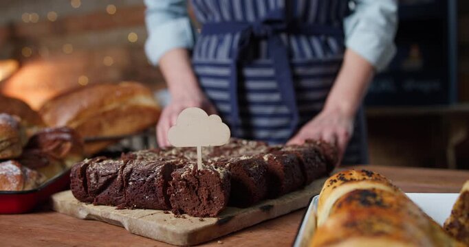 Female Sales Assistant In Bakery Putting Blank Label Into Chocolate Brownie
