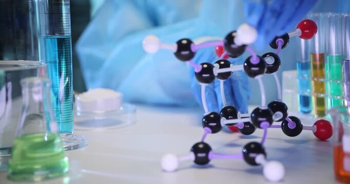 Scientist hand holds molecular structure model on laboratory table. Chemist in protective gear conducts experiments with fluids in laboratory