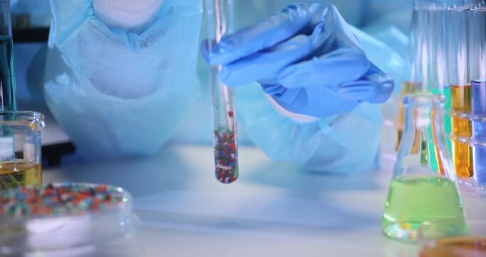 Chemist hands stir particles of microplastic in test tube over lab table. Technician analyzes polymer pollutants reaction on water in laboratory