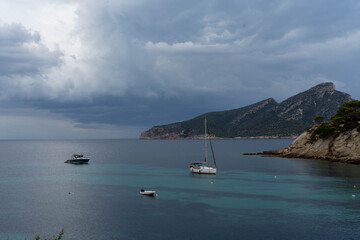 Storm clouds over tranquil bay with anchored sailboat and turquoise water © Palina Kuchur
