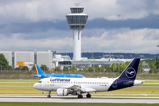 Ein Airbus A319-100 der Lufthansa rollt auf dem Rollfeld vor dem Tower. Im Hintergrund ist ein Flugzeug der ITA Airways zu sehen, dem neuen Partnerunternehmen der Lufthansa Group.
