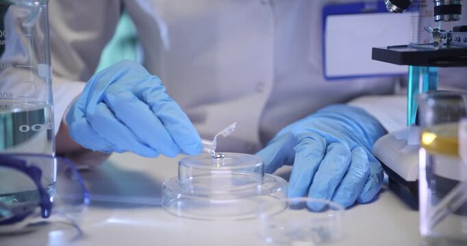 Woman scientist pours metallic liquid onto glass podium in chemical lab. Technician researches silver substance with modern equipment on table