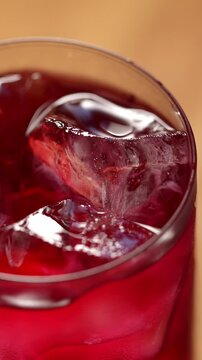 Ice cubes swirl in a glass of berry sparkling kombucha, top view. Iced fizzy drinks, and summer vibes.