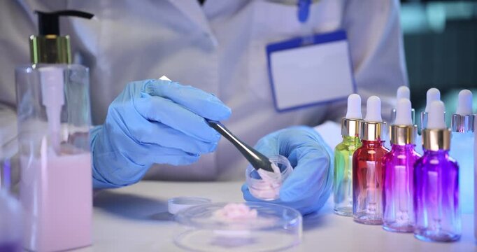 Medical specialist places cream from Petri dish into small jar on lab desk. Dermatologist tests different cosmetic products in laboratory slow motion