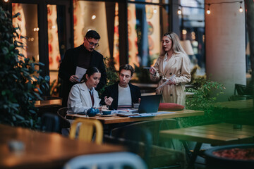 A small business team meets at an outdoor cafe, reviewing documents and working on a laptop....