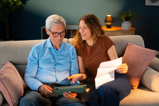 Adult daughter assisting elderly father with financial documents and digital banking services at home.
