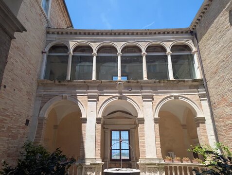 Un elegante chiostro storico a Fermo, con archi sovrapposti e colonne in pietra, crea un&rsquo;atmosfera armoniosa e luminosa che richiama l&rsquo;architettura classica dei palazzi rinascimentali della citt&agrave;