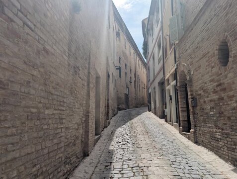 Vicolo in pietra dal fascino antico sale tra edifici storici in mattoni, illuminato dalla luce del sole che crea un&rsquo;atmosfera tranquilla e autentica tipica dei borghi europei