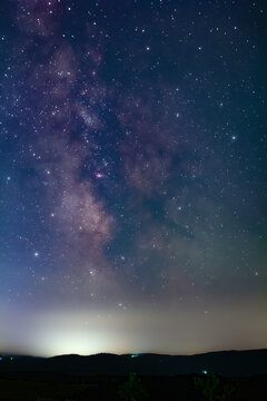 Constellation and Milky Way stars on a dark countryside skies with landscape silhouettes.