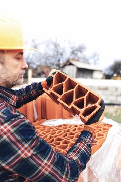 Bricklayer mason holding a regular brick outdoors on a construction site.