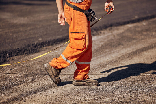 Construction worker using tape measure to measure dimensions of the street during reconstruction.