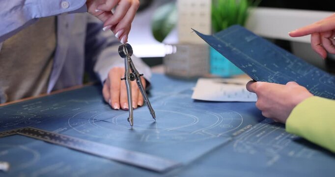 Woman designer draws circle with compass on blueprint as colleague checks plan in office. Female engineers work on project in architectural bureau