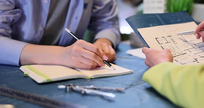 Manager writes in notebook as assistant holds building plan in office. Female architect designers develop construction project in agency slow motin