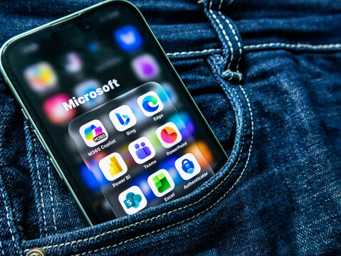 Smartphone in a denim jeans pocket displaying a microsoft app folder with various icons including m365 copilot, bing, edge, teams, and excel