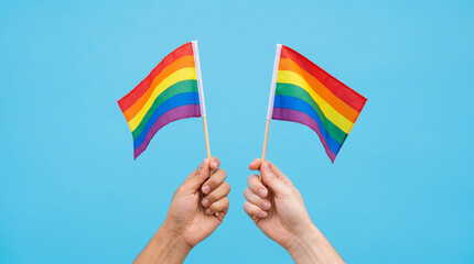 Fototapeta premium Two hands confidently holding rainbow flags on a bright light background, concept of pride, equality, support for the LGBTQ+ community and human rights, celebration of Pride Month