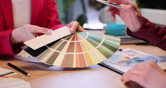 Female interior designer shows color swatch fan to client in company office. Woman expert helps customer to choose style of home decor slow motion