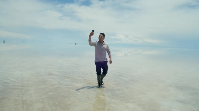 A Latino man on vacation with his cell phone in the Uyuni Salt Flats, with the mirror effect, in Potos&iacute;, Bolivia