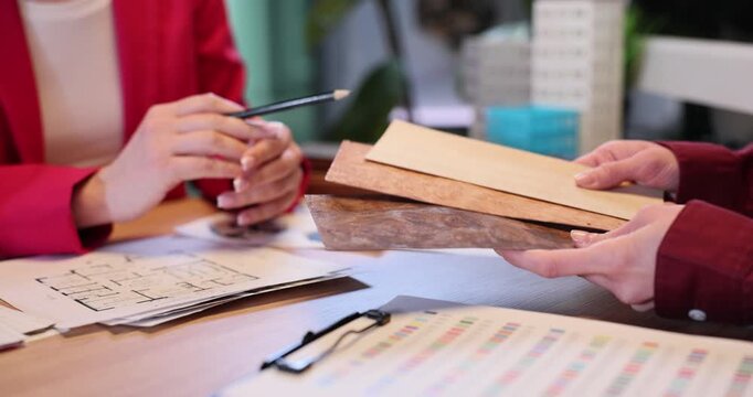 Customer holds wooden panel samples as designer gives advice in office. Female expert explains difference between lamber types to client slow motion
