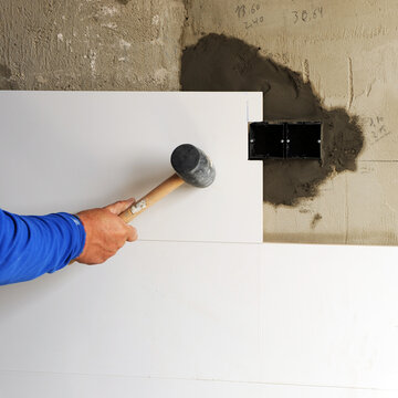 Primer plano de la mano de un alba&ntilde;il con un mazo de goma en la mano ajustando los azulejos de gres porcel&aacute;nico blanco en la renovaci&oacute;n completa de la cocina de una vivienda