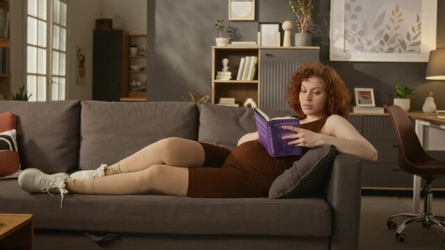 Pregnant Caucasian young adult woman lying on sofa and reading book while wearing compression stockings. Clip ideal for maternal healthcare and prenatal wellness marketing