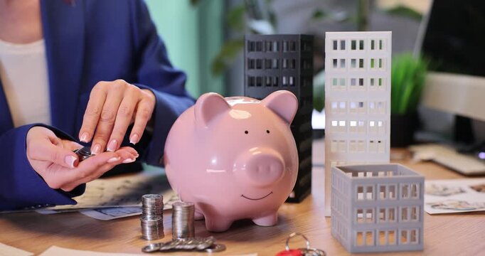 Businesswoman puts coins into piggy bank collecting money for real estate in office. Female broker offers loan for apartment buying slow motion