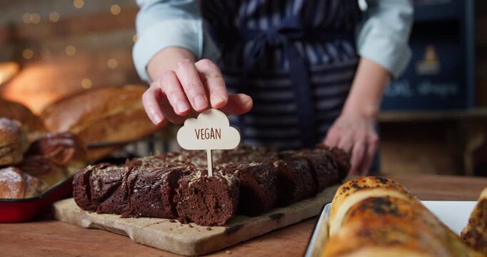 Female Sales Assistant In Bakery Putting Vegan Label Into Chocolate Brownie