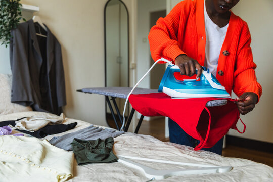 Young Black Woman Ironing Laundry on Board in Bedroom