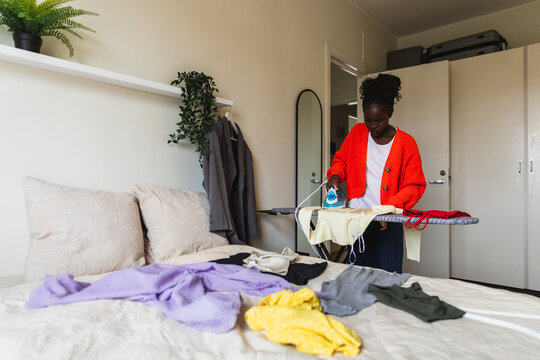 Young Woman Ironing Clothes on Board in Bright Bedroom