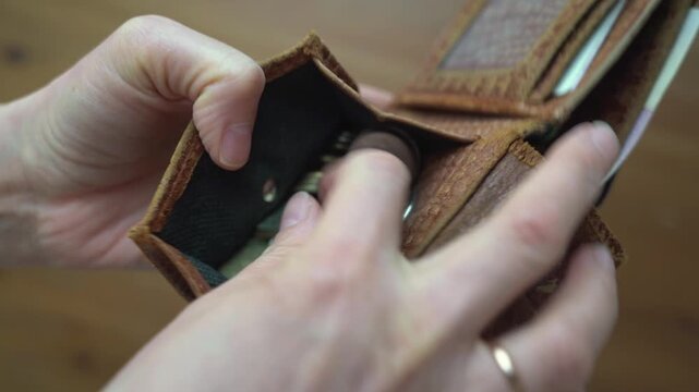 Close-up of hands opening a brown leather wallet, revealing an empty card slot, followed by coins inside, and finally adjusting the wallet's contents in a cozy indoor setting